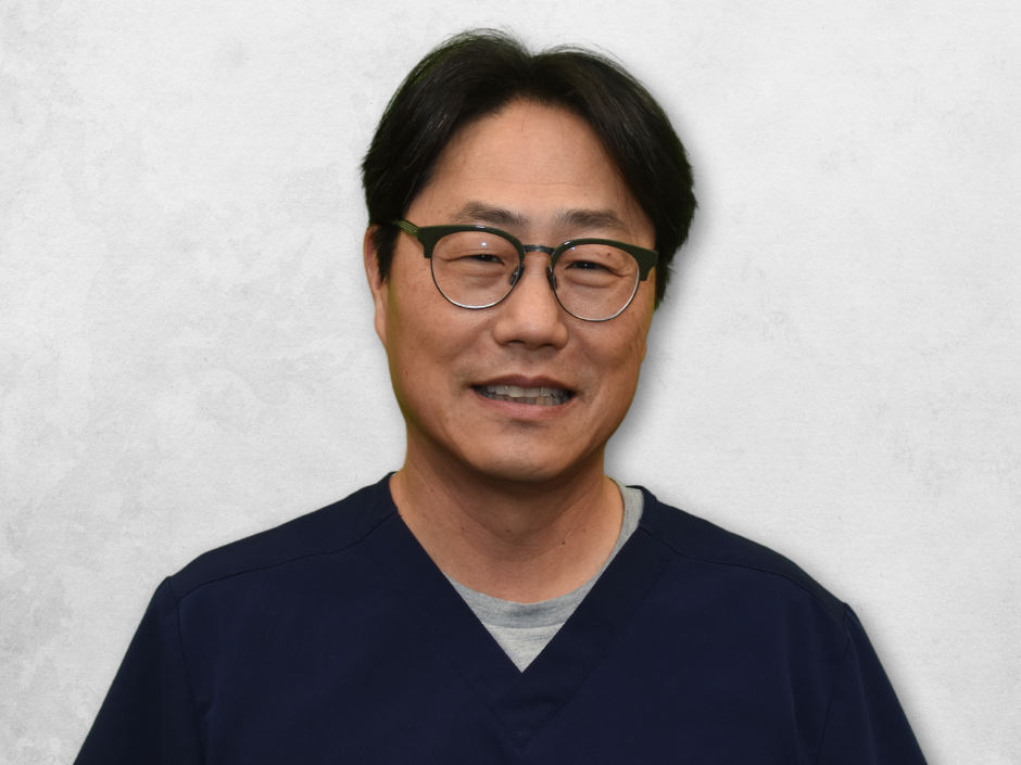 Dr. Kim is wearing navy blue scrubs and has glasses